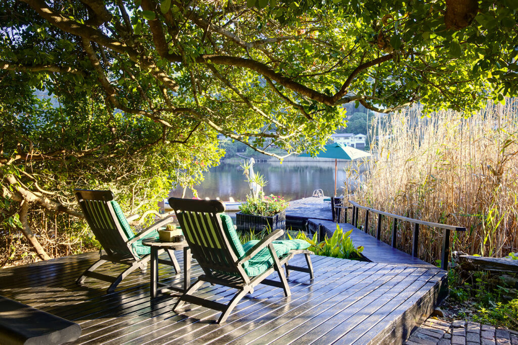 two loundgers on a wooden deck under a tree alongside a river, a prime example of what the Wilderness accommodation has to offer