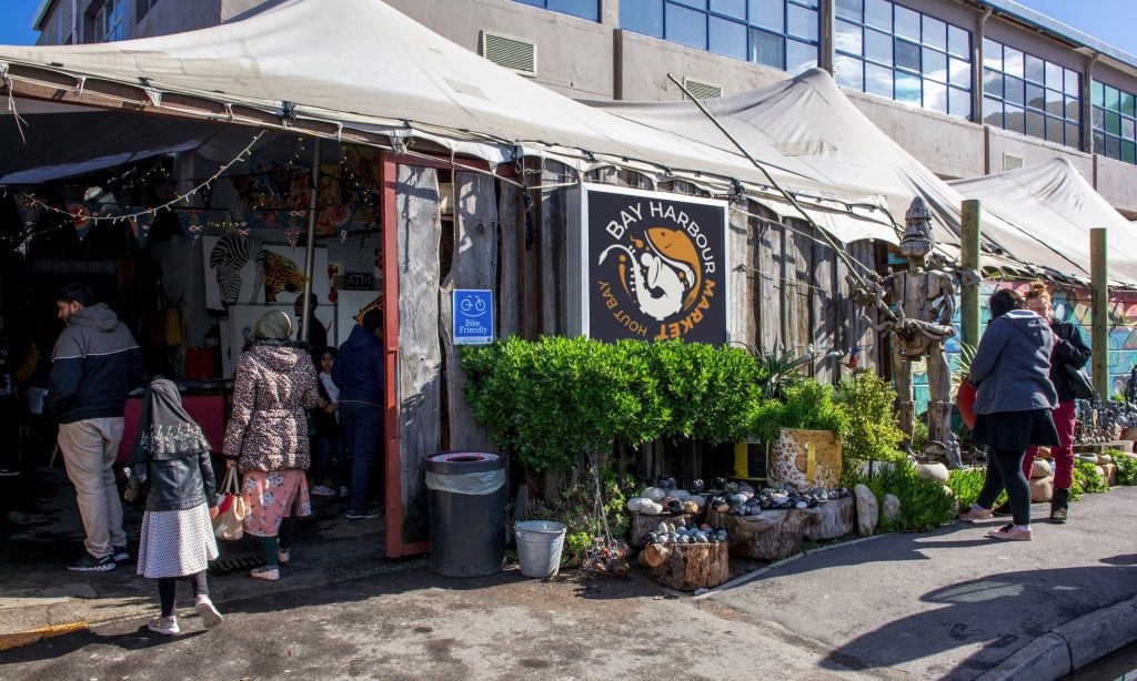 The Bay Harbour market entrance, canvased roofs slope away from the large warehouse building, and driftwood planks make walls for this covered Hout Bay market