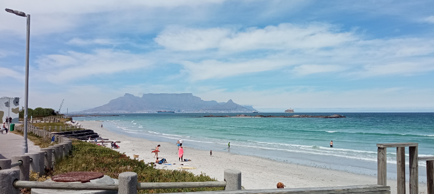 lively beach looking over the blue atlantic ocean, Table Mountain can be seen across the bay, another prime example of the beauty of Cape Town beaches