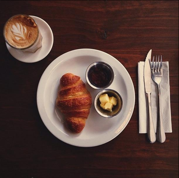 a croissant with spreads alongside  and coffee on a saucer, an example of a breakfast Cape Town has to offer
