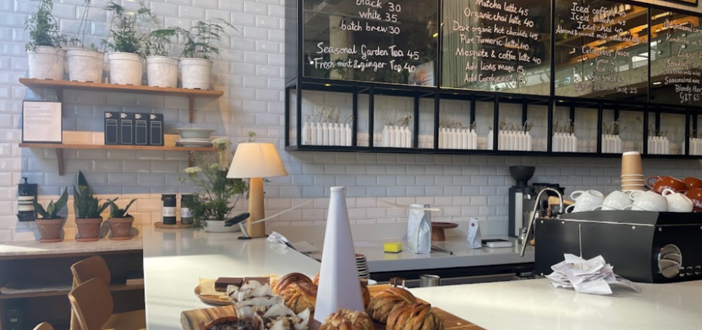 Pastries arranged on a board atog a white counter, white brick wall of the building extends behind the bar, menus on boards and various pot plants adorn the wall, breakfast Cape Town