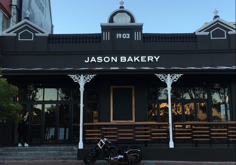 A historic building painted a stylish black, a cruiser motorcycle stands outside this establishment, another stylish place for breakfast Cape Town has to offer