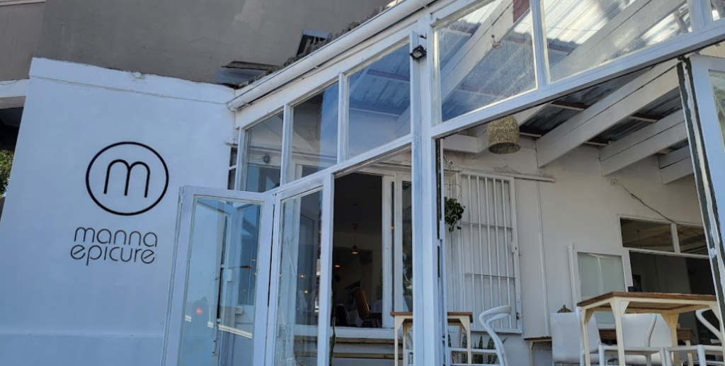 Stylish glass sunroom outside the restaurant, the M logo of manna epicure on the white wall, another great place for breakfast Cape Town has to offer