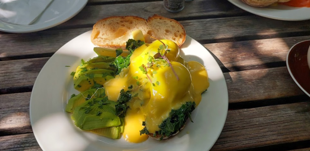 A beautiful breakfast, egg on bread covered in hollandaise sauce, with avo beautifully arranged alongside it, an example of the type of breakfast Cape Town has to offer