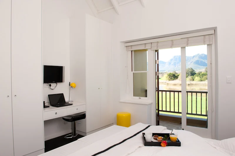 A stylish contemporary room with a double bed, and small desk, outside the doors a small terrace is visible, with mountain views, an example of what this Paarl accommodation has to offer