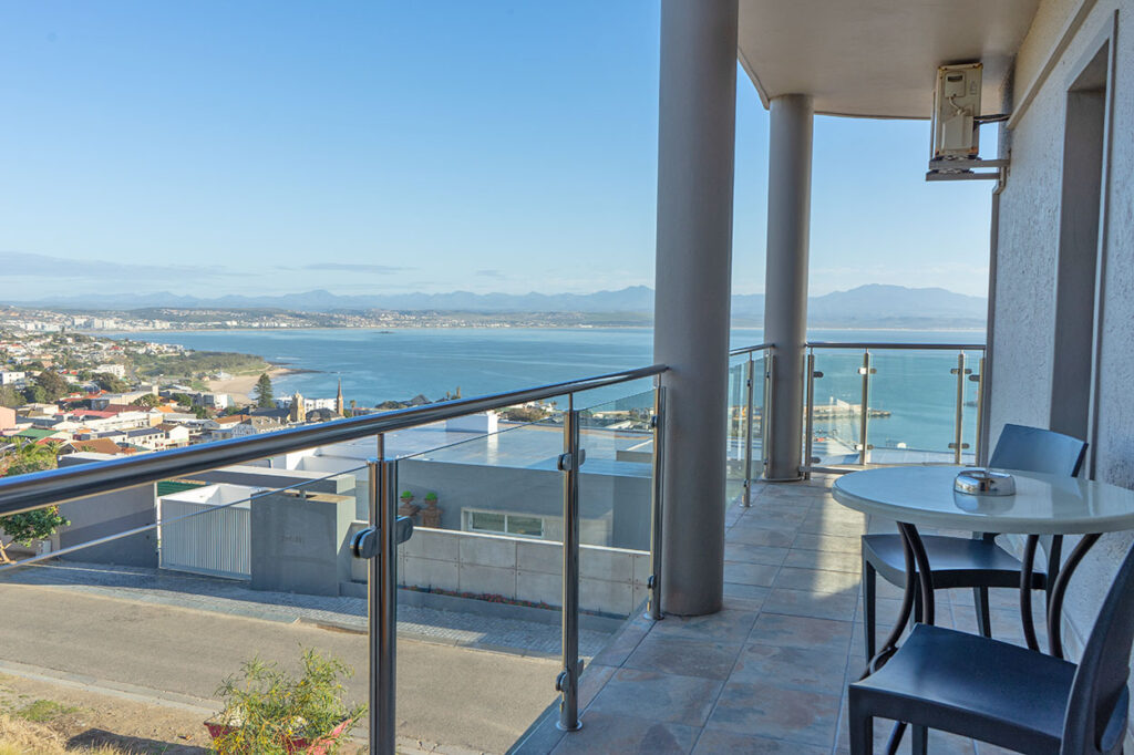 Guesthouse balcony overlooking the town and bay, a simple table with 2 chairs are on the balcony, a great place to unwind at this accommodation at Mossel Bay