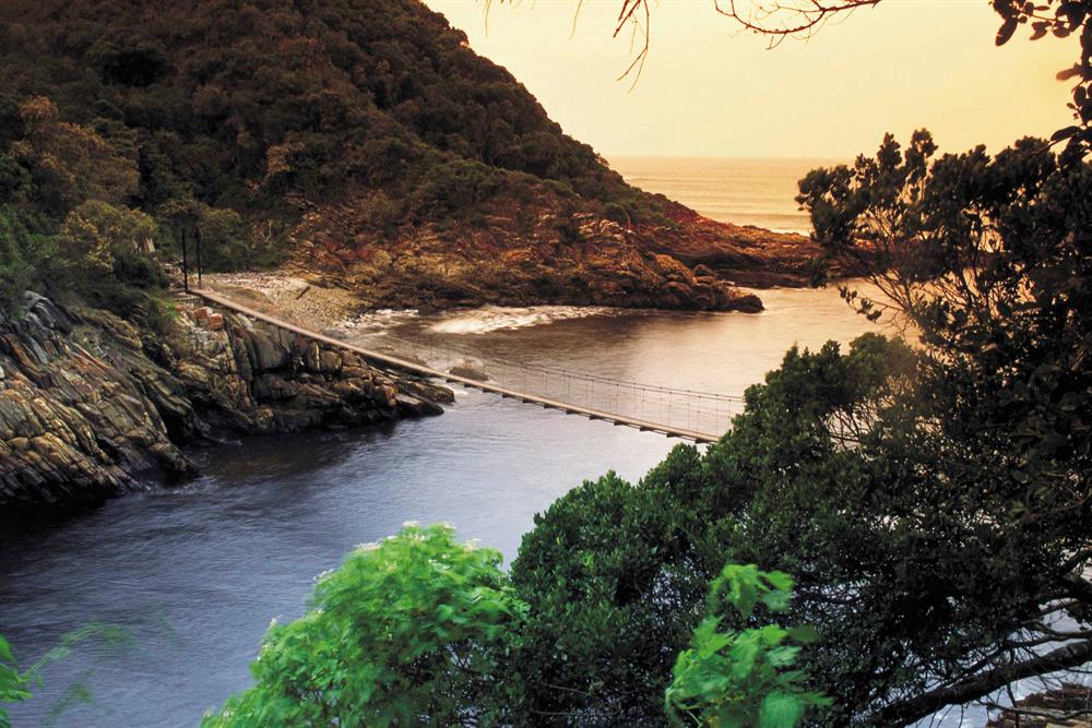 A rope bridge crosses the river, and on this bank lush trees are visible, while across the river you can see a mountain, another great SAN park to visit