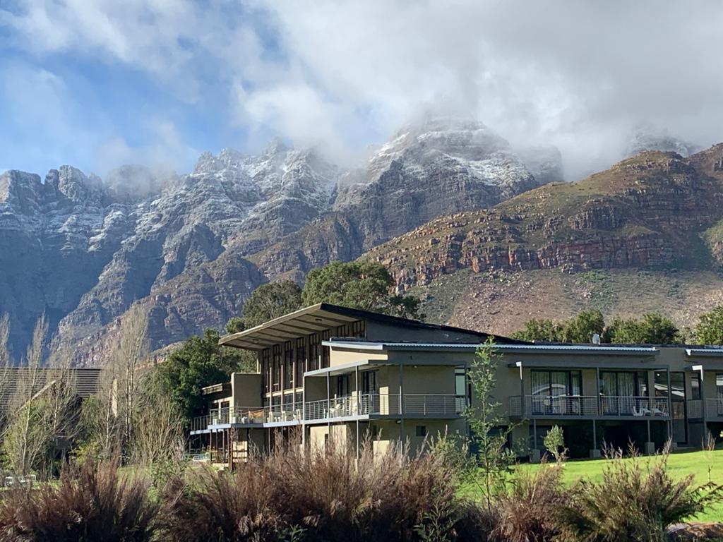 The main lodge of this Paarl accommodation, is a contemporary building, with green lawns in front of it, and mountains looming behind it.