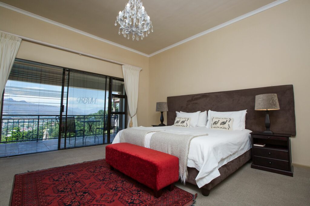 Beautifully furnished bedroom with a double bed, Large glass door leads out to a terrace with table and chairs, with views of the mountains in the distance, an example of what Paarl accommodation has to offer