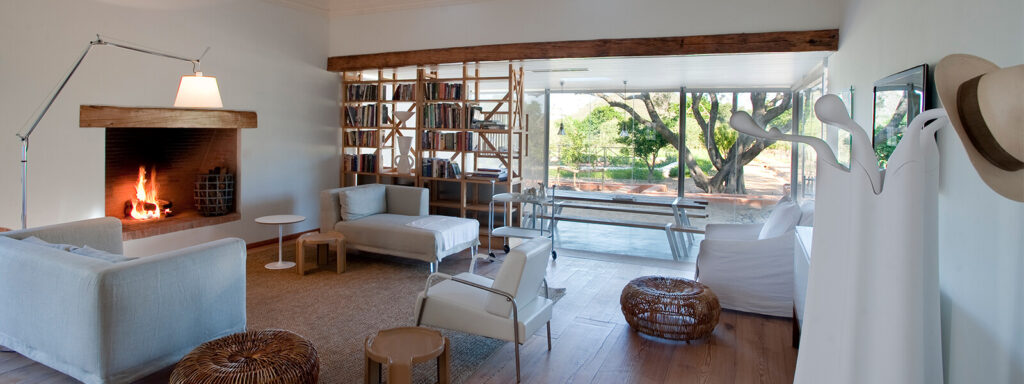 A beautiful room at this Paarl accommodation, with wooden floors, white walls and furniture, a lovely fireplace, and a tree seen through the large glass doors